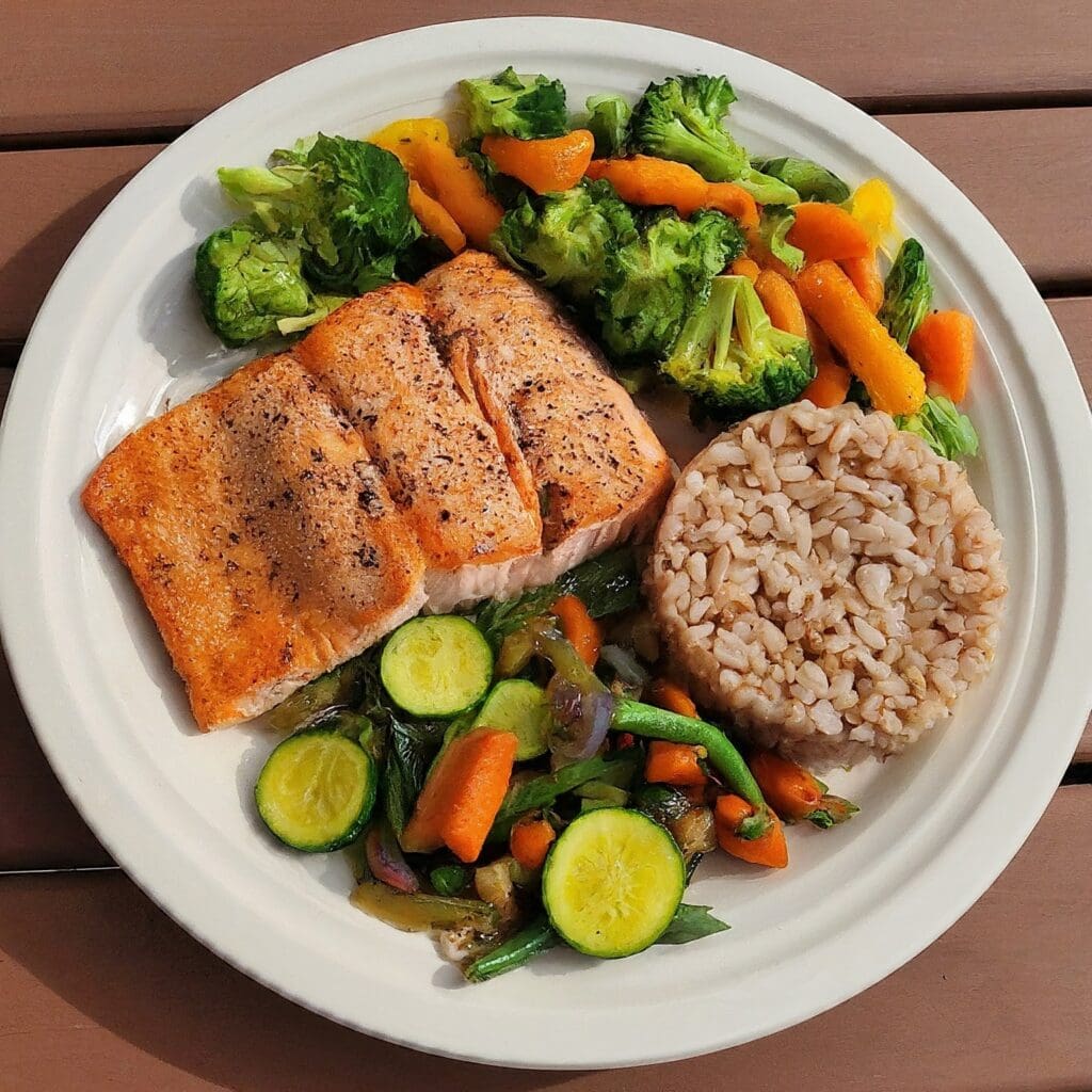 A colorful plate filled with a balanced meal including grilled salmon, steamed vegetables, brown rice, and a side salad with olive oil dressing. This represents a heart-healthy diet recommended for managing hyperlipidemia