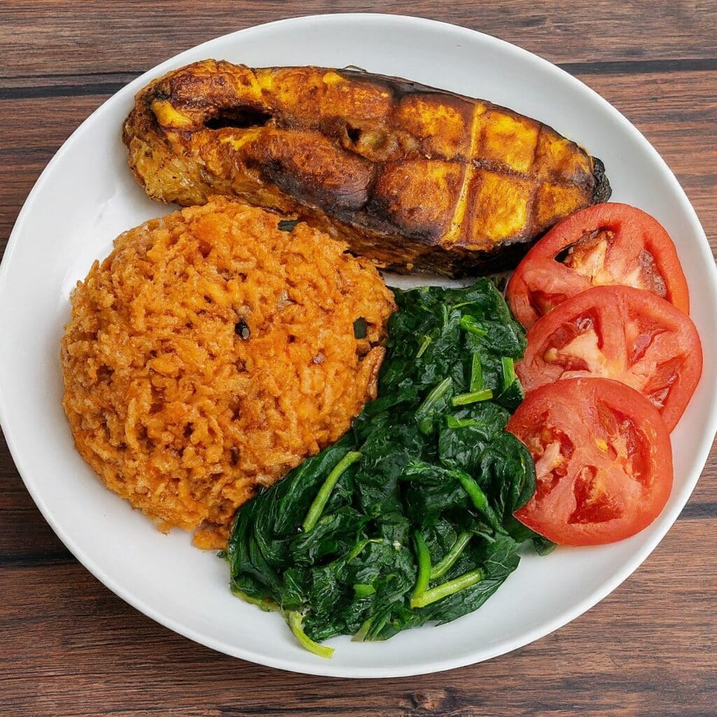 A plate of Nigerian food which consists of Jollof-rice, grilled fish, and steamed vegetable with sliced bell tomato. A combination of Nigerian diets for weight loss